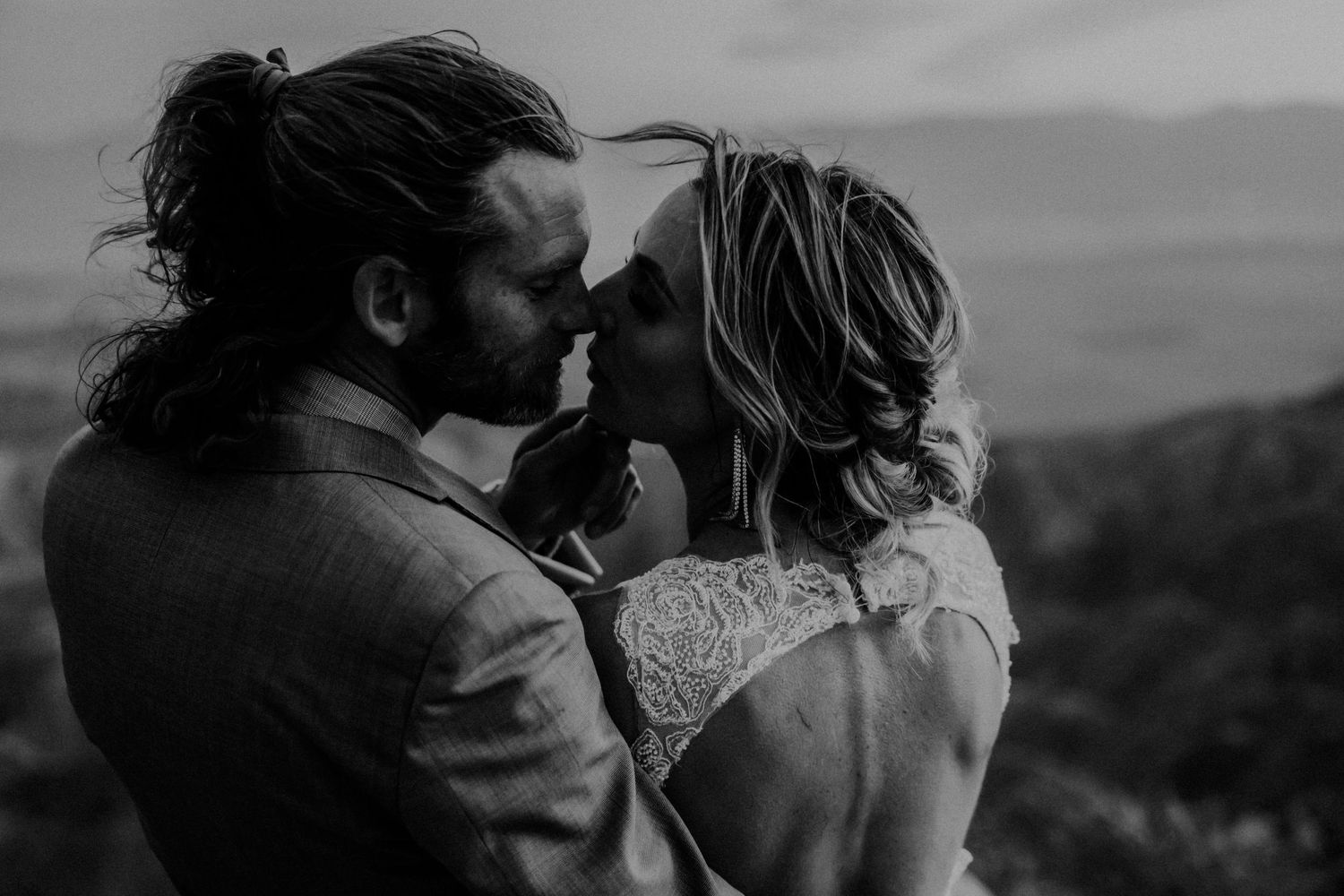 Black and white silhouettes of a romantic couple embracing against a scenic mountain backdrop.
