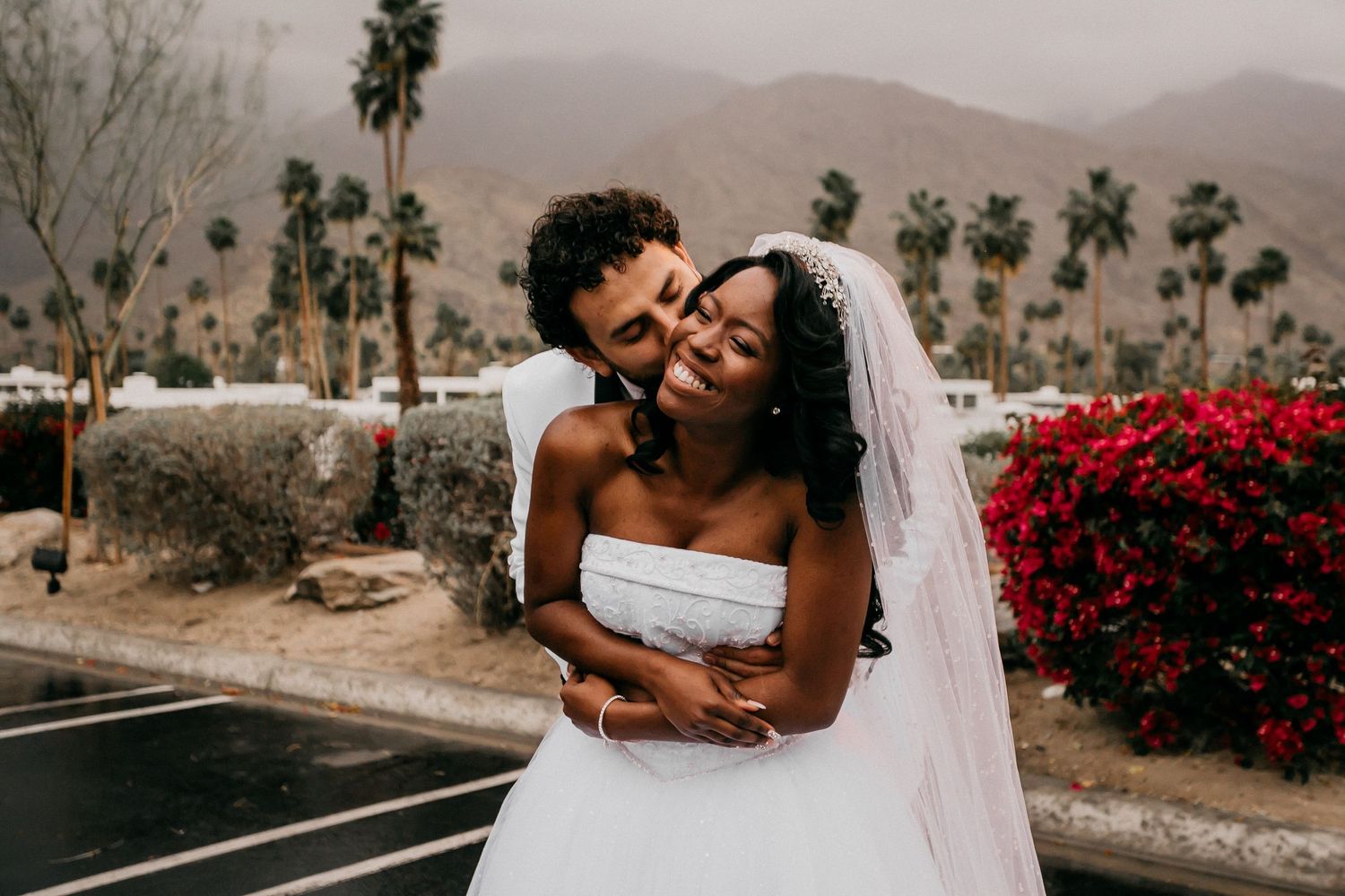 Desert wedding photo series at sunset shows couple in intimate embrace among desert flora and red flowers.