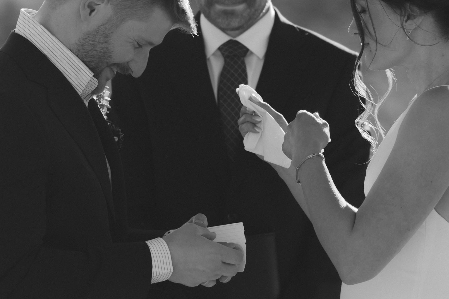 Black and white photo of a groom placing a wedding ring on the bride's finger during a ceremony.