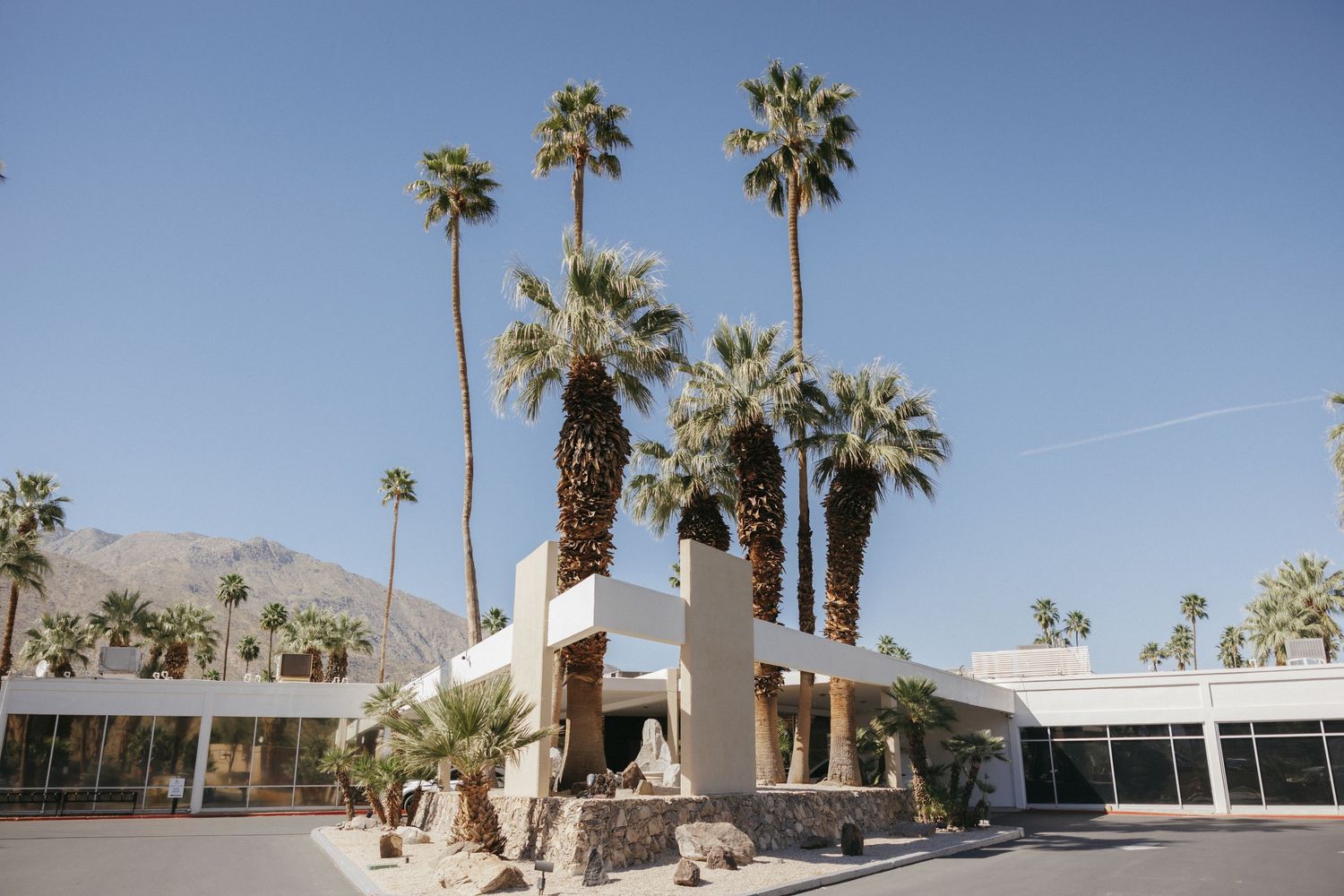 Mid-century modern hotel with tall palm trees and mountain backdrop under clear blue sky in Palm Springs.