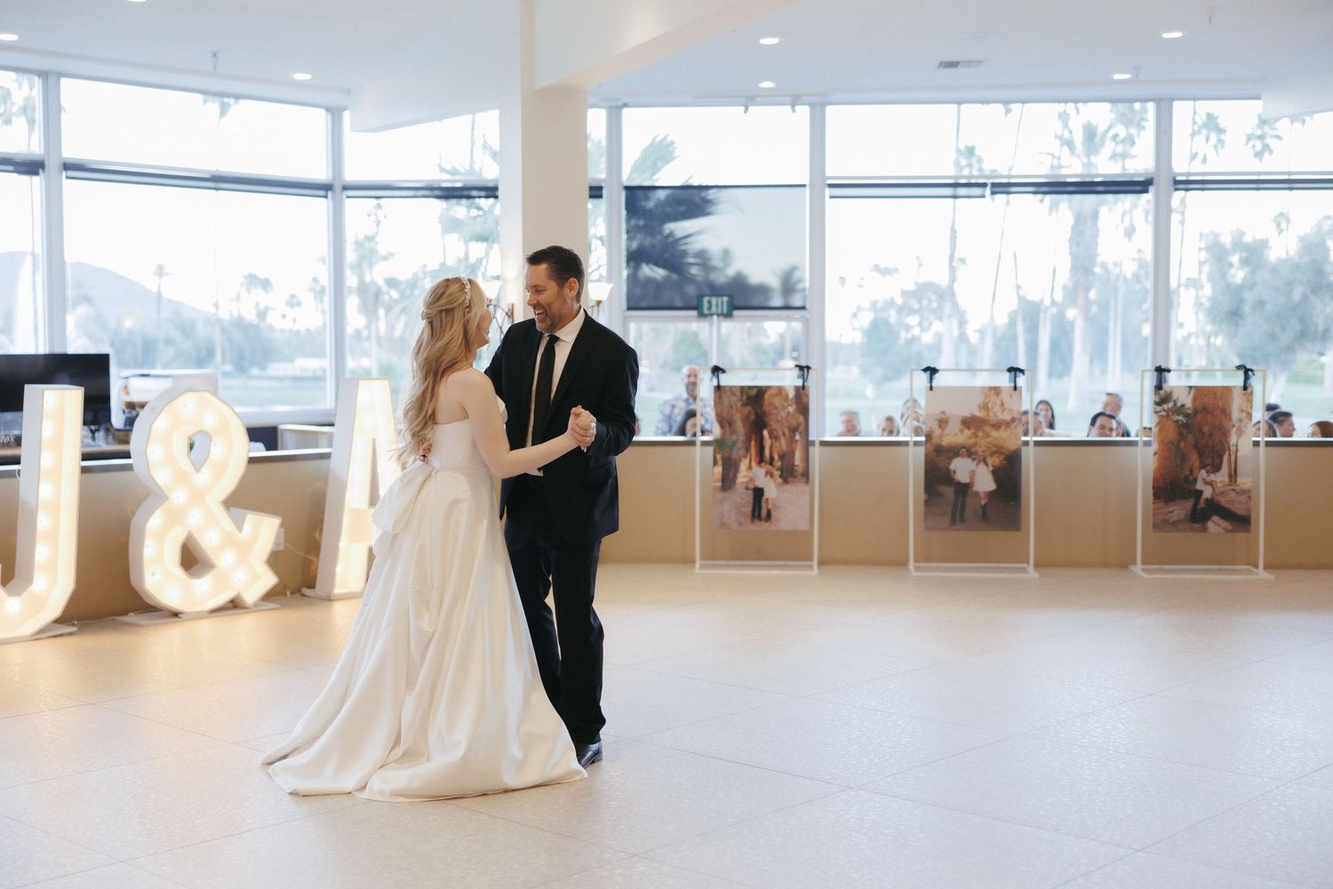 Bride and groom share first dance near large marquee letters and framed photos in modern reception venue.