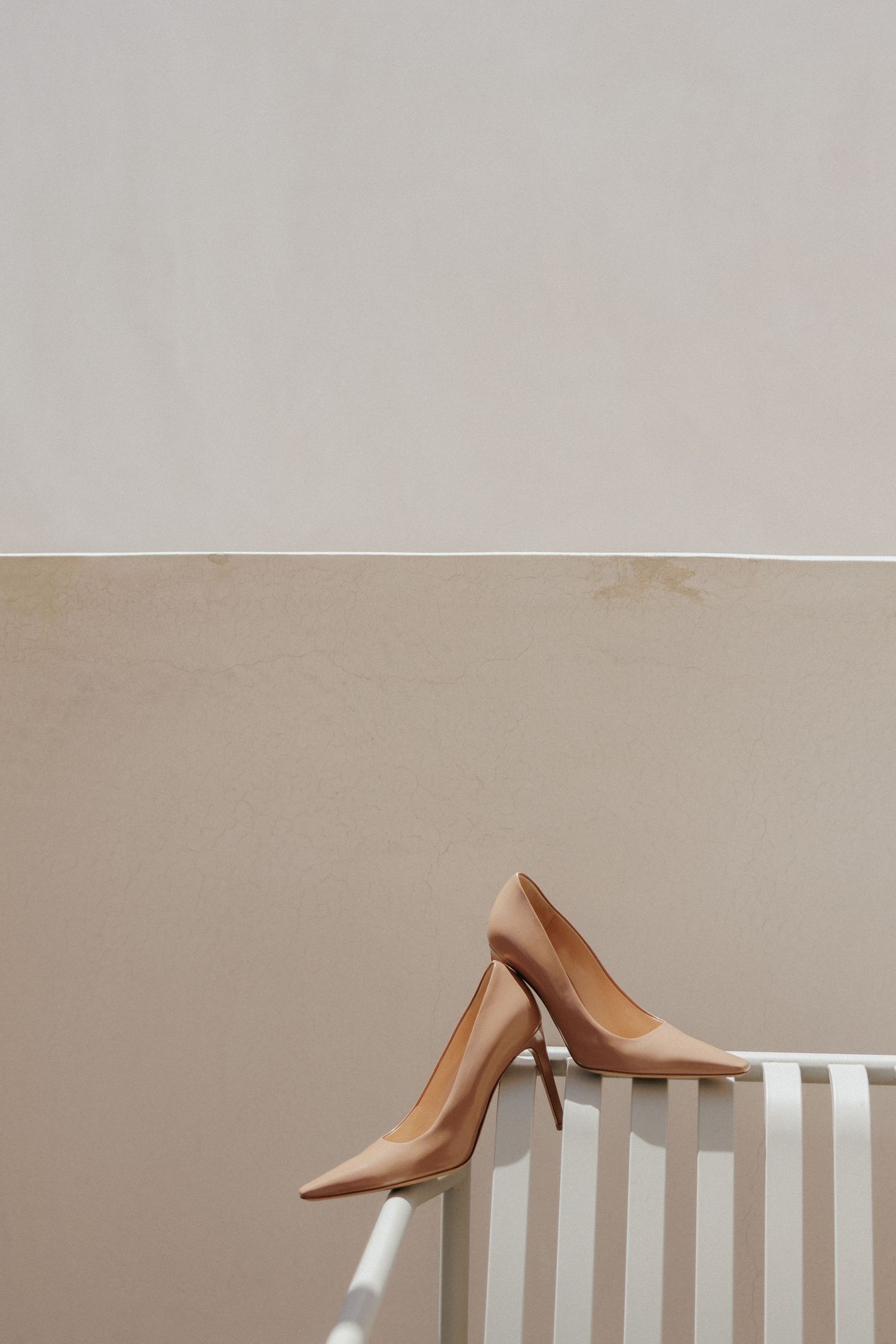 A nude colored high heel shoe rests elegantly on top of a white bench.