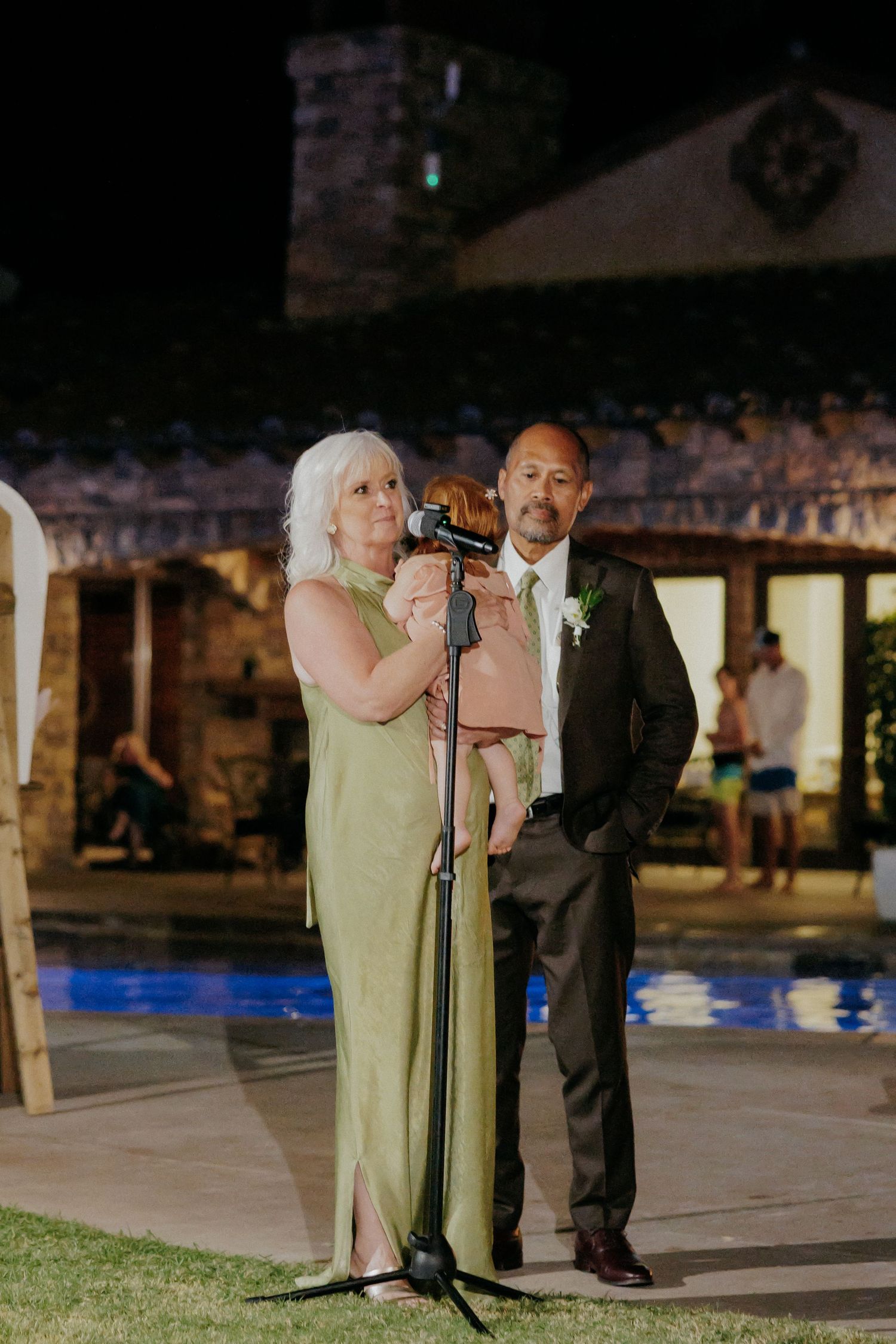 A light green wedding dress flows in the evening breeze as a couple stands together during an outdoor reception.