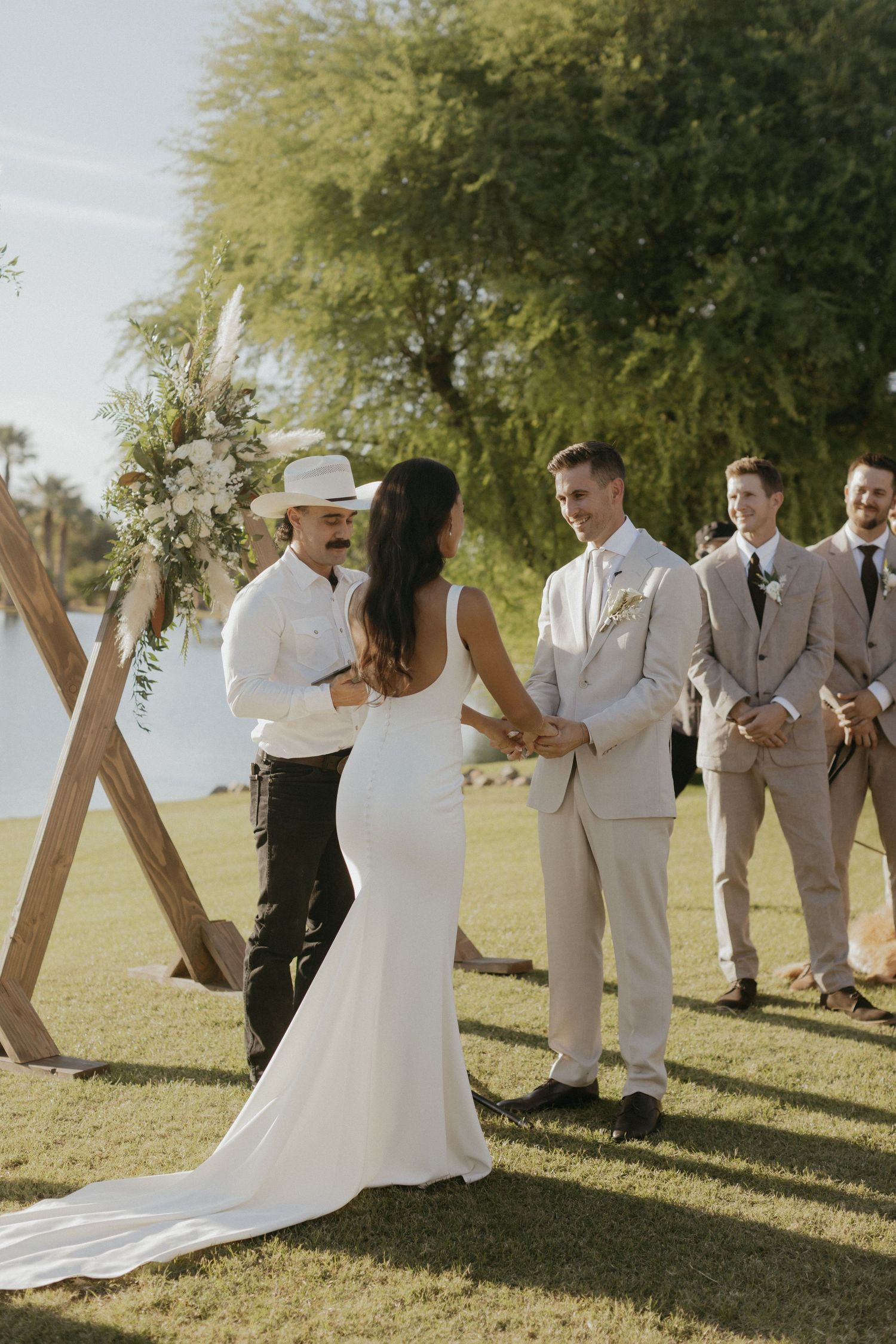 Newlyweds and wedding party celebrating outdoors under trees in modern grey and white attire during sunset.