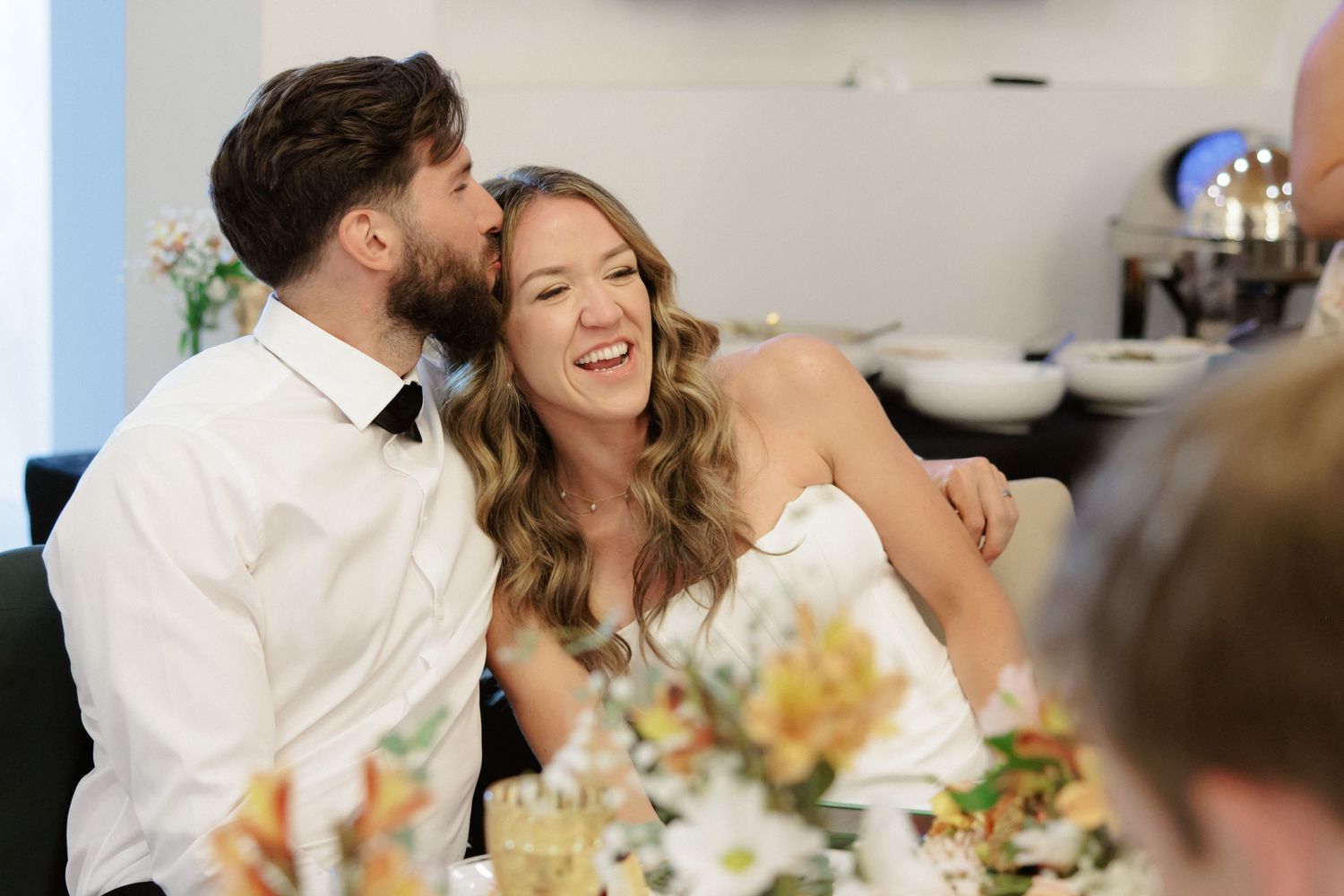 Candid moments of joy and laughter shared during a wedding reception among guests at a decorated dining table.