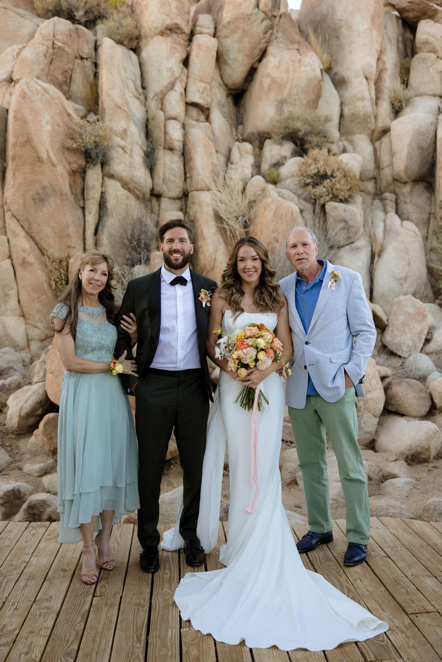 Wedding party poses in front of dramatic rock formations on wooden deck in natural outdoor setting.