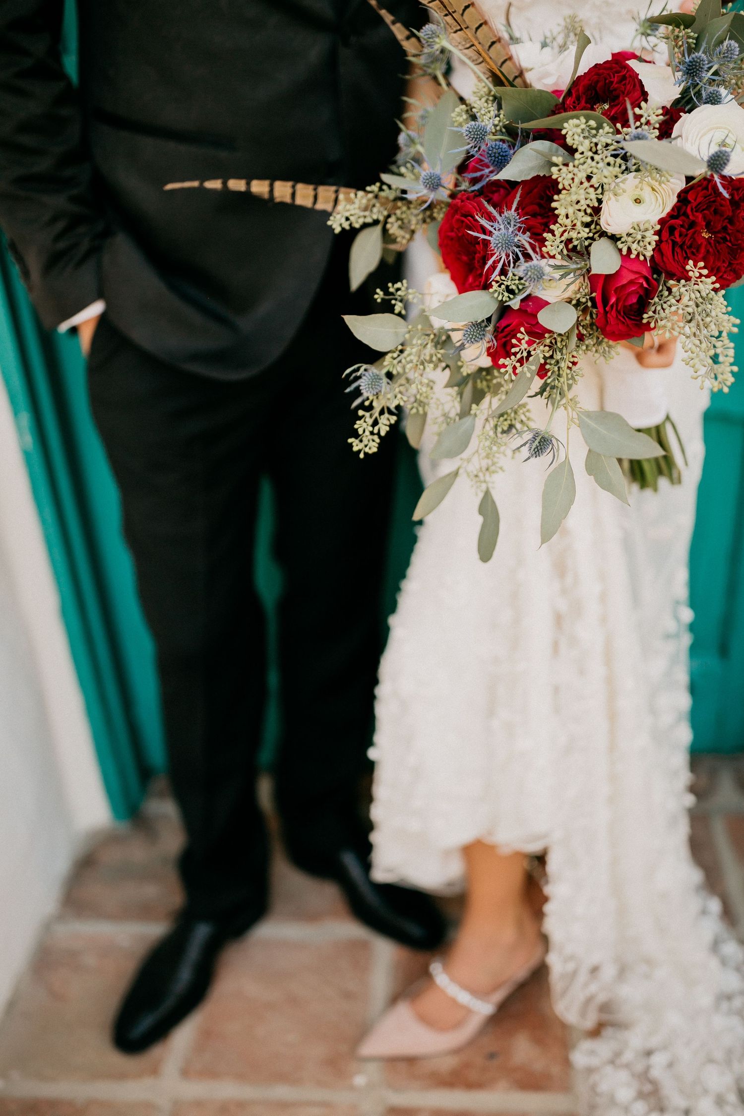 Wedding party members stand close together while displaying elegant bouquets with red and white flowers.