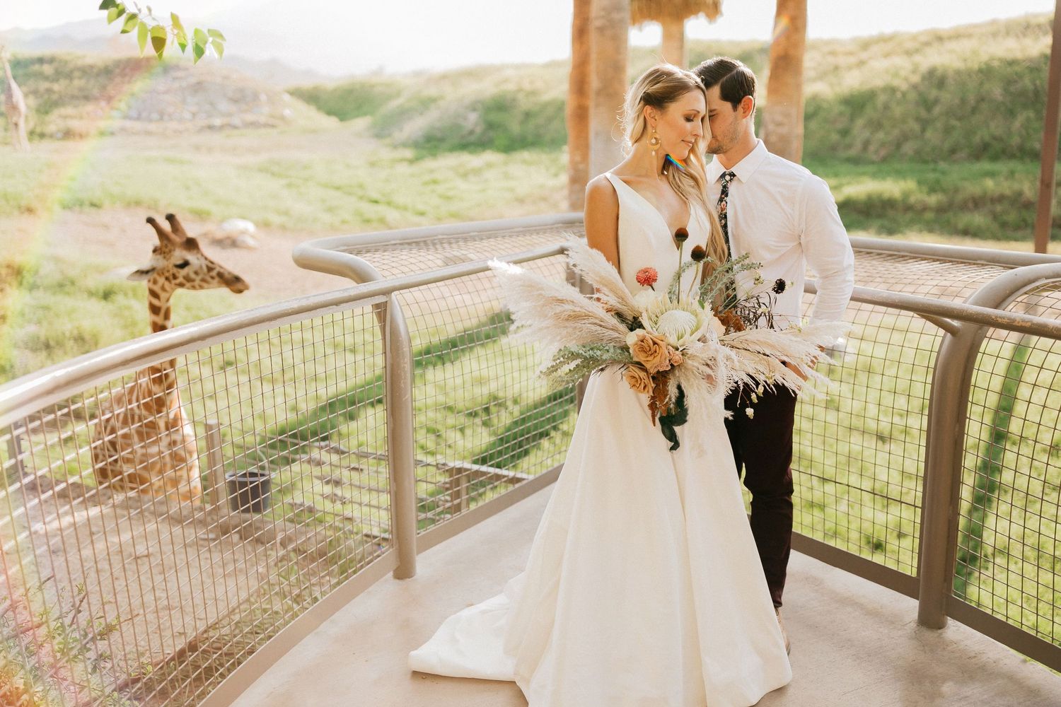 Couple shares a romantic moment along wooden railing overlooking scenic natural landscape at sunset.