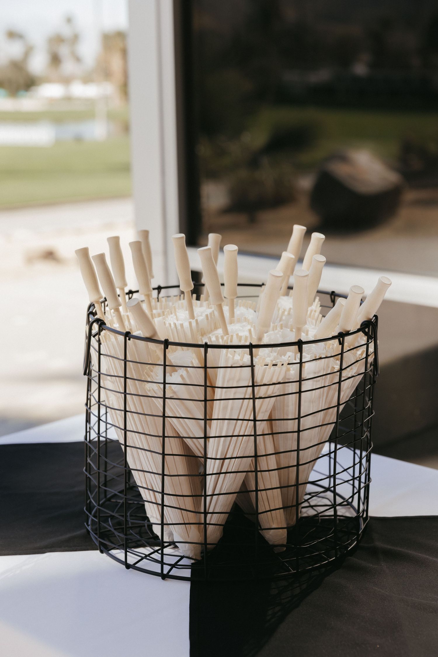Wire basket filled with hand-held paper fans with wooden handles for wedding guests.