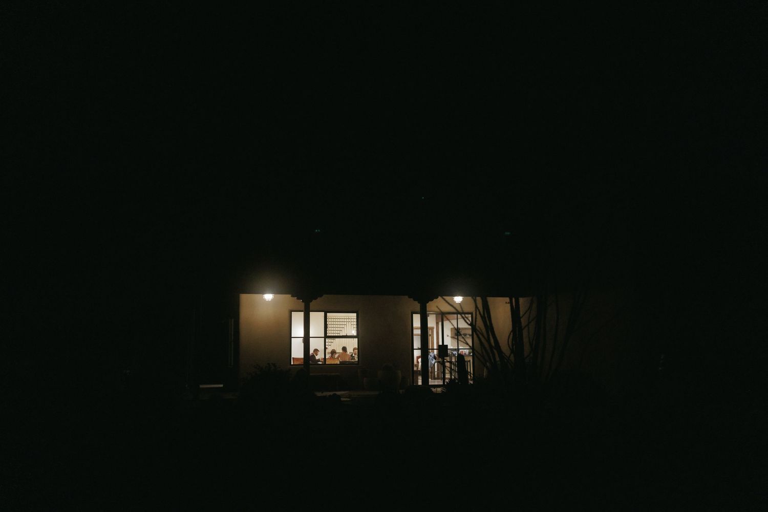 Warmly lit house exterior at night with wedding guests visible through glowing windows.