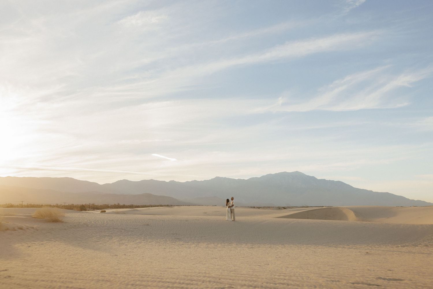 A couple walks across vast white sand dunes at White Sands National Park with mountains and golden sunset sky.