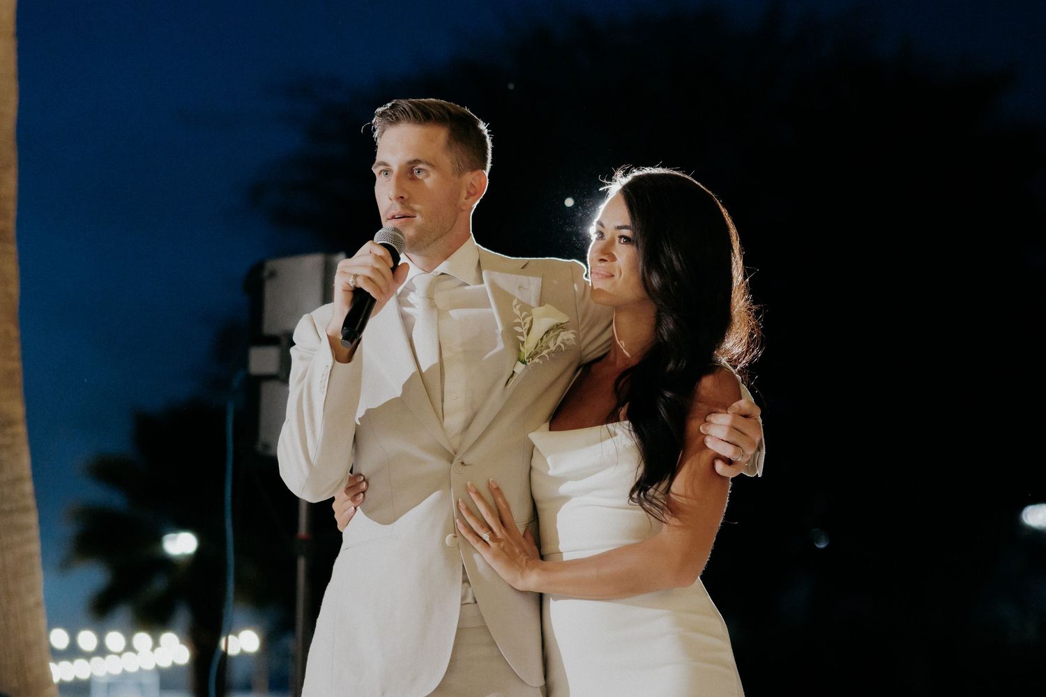 A couple in elegant cream-colored outfits share a romantic dance together at an evening reception.
