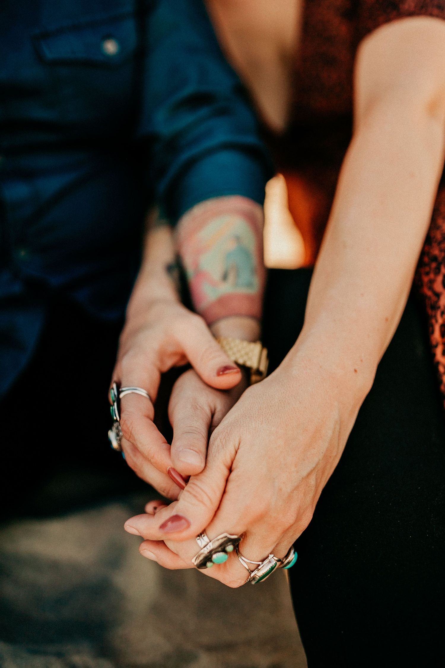 Close-up of intertwined hands with rings and a visible tattoo on one arm.