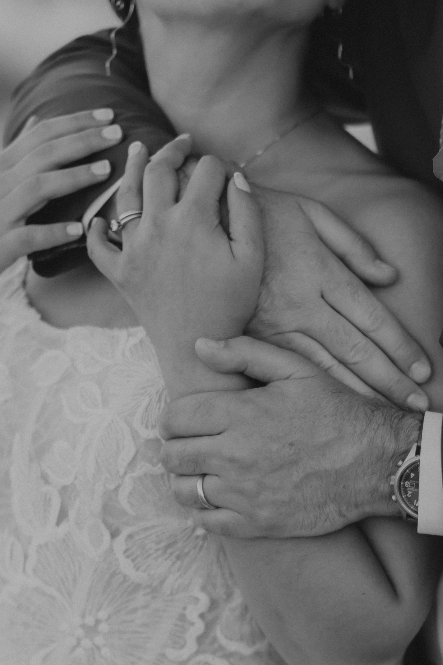 Close-up of two hands clasped together against white lace fabric in black and white style.