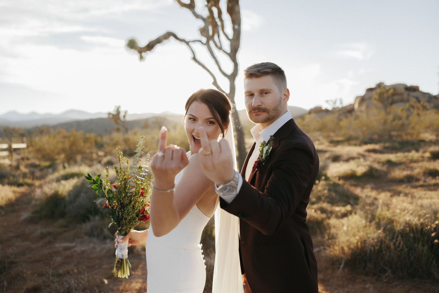 Bride and groom show off wedding rings smiling in Joshua Tree desert at sunset.