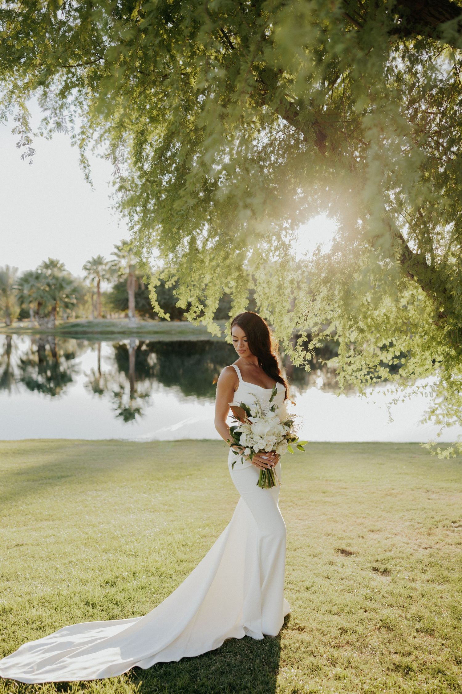 Bride in flowing white gown twirls gracefully in a sunlit garden setting during golden hour photography session.