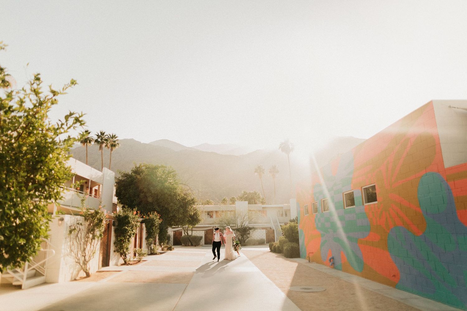 A sun-drenched street with colorful murals and palm trees during sunset in a desert town.