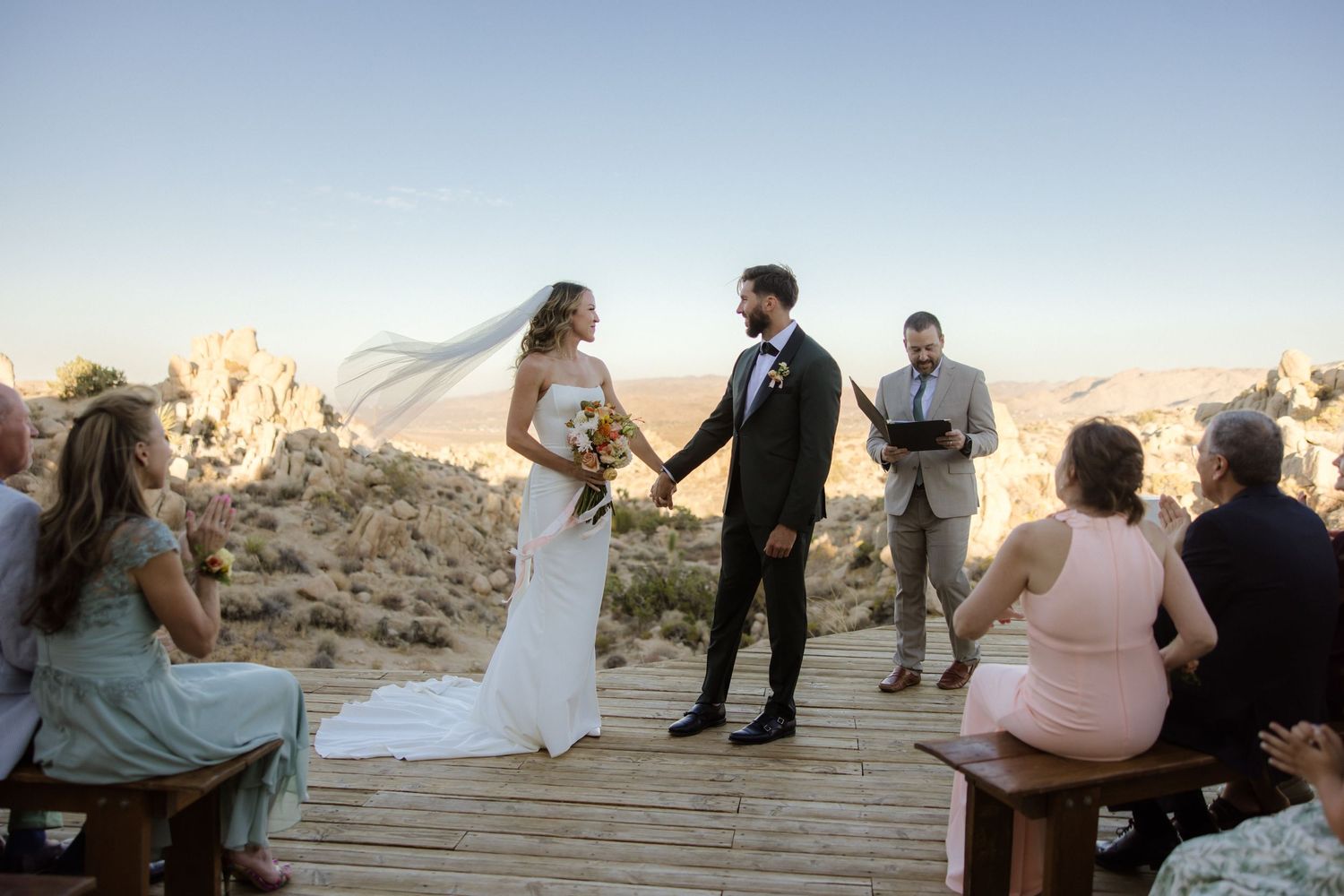 Golden hour wedding ceremony in front of rugged desert cliffs creates a romantic ambiance with warm sunlight.
