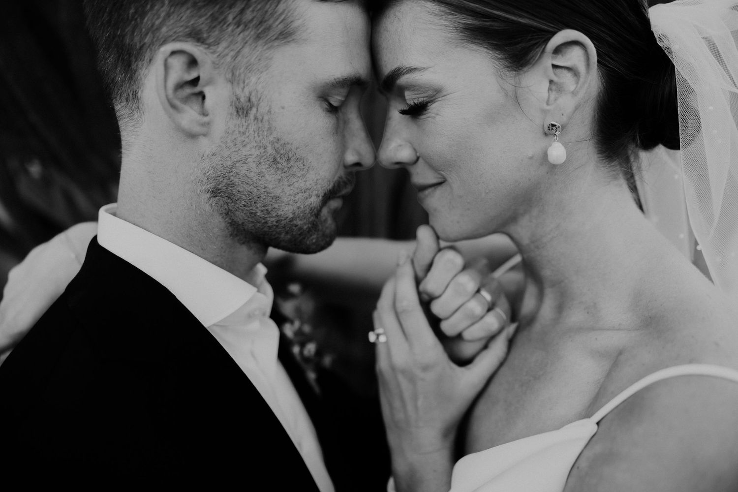 Black and white wedding photo of bride and groom sharing an intimate moment, touching foreheads tenderly.