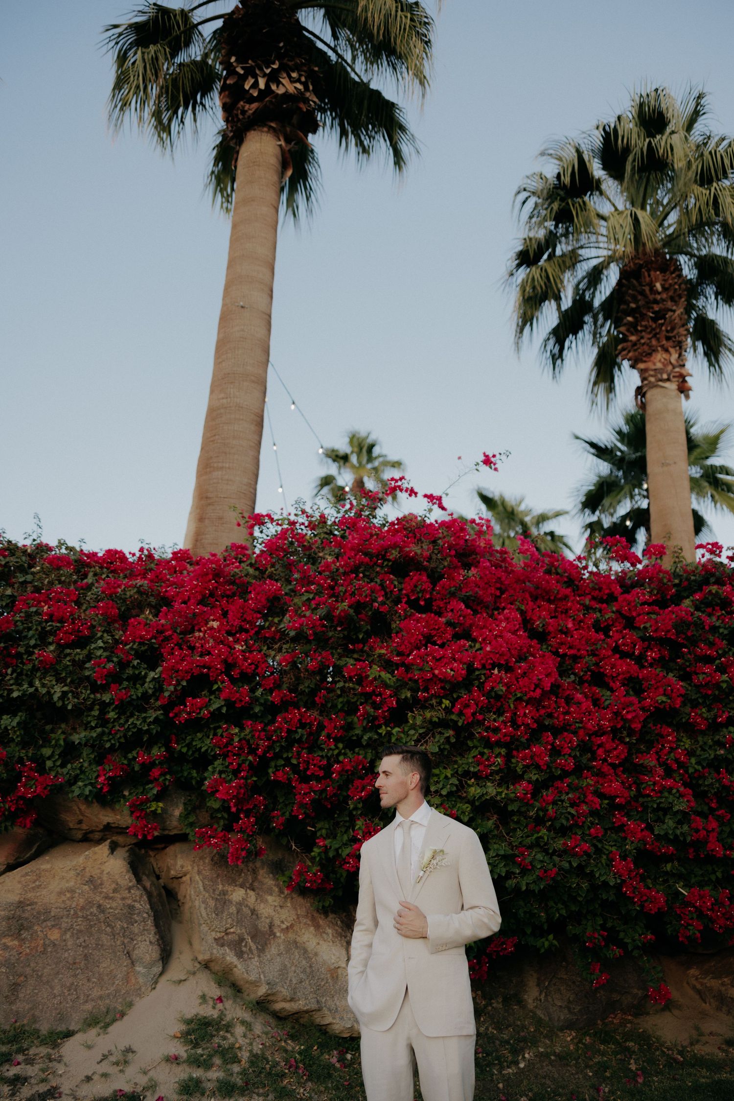 Photography sequence against red bougainvillea and palm trees showing someone in white suit posing from different angles.