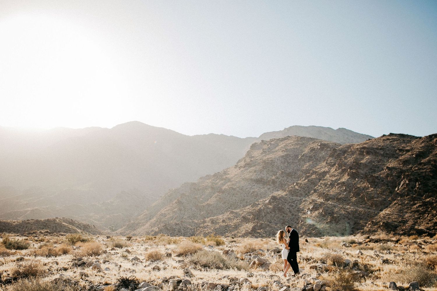 Wedding couple silhouetted against a mountainous desert landscape.