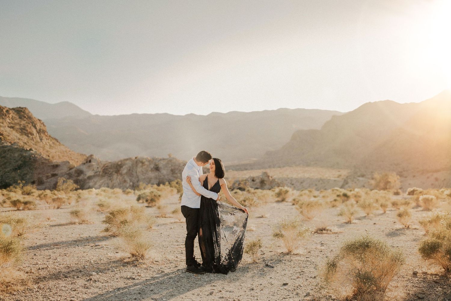 Golden sunset light illuminates a romantic desert photoshoot with mountains in the background.