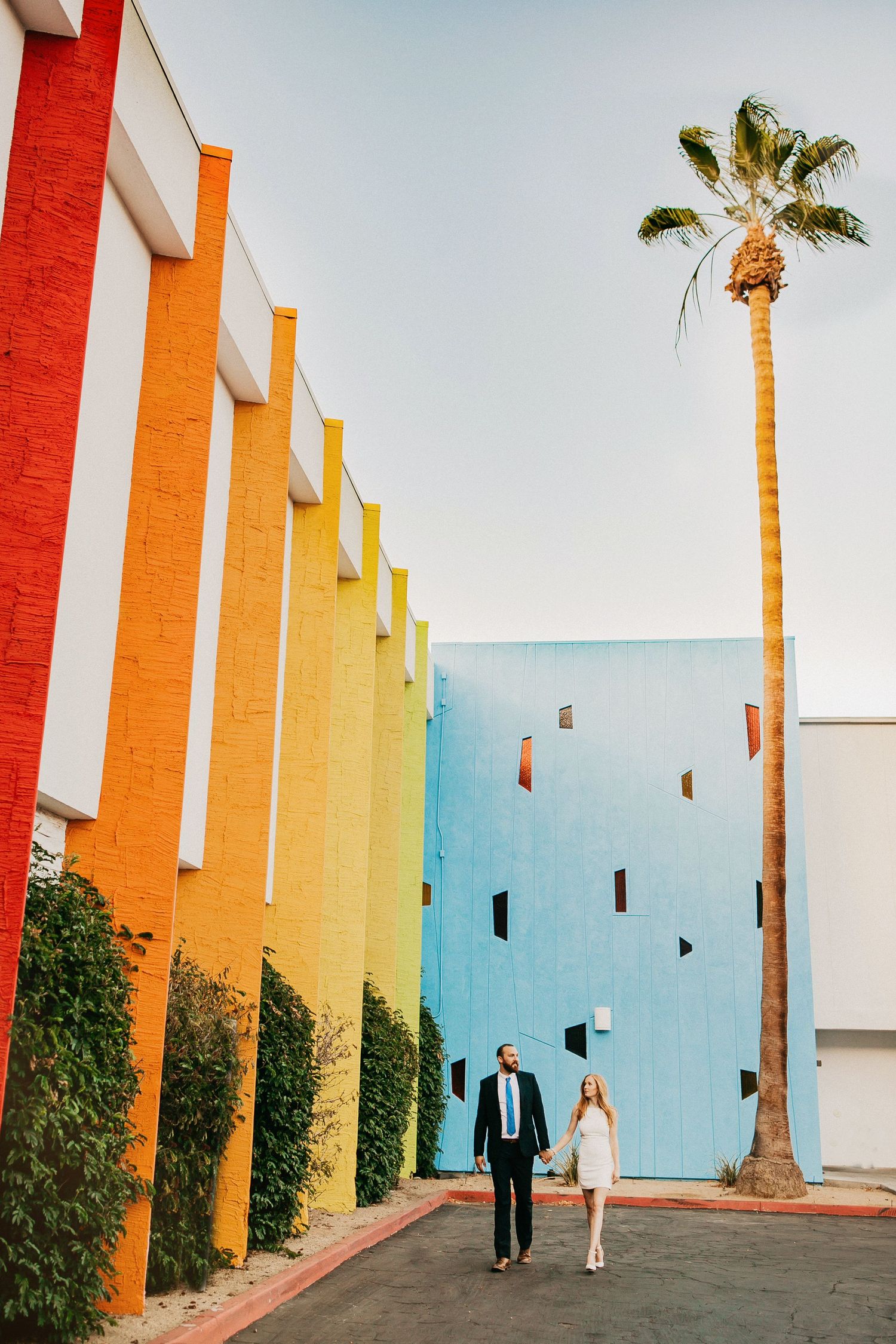 Colorful striped columns in orange and yellow hues line a walkway with palm trees against a blue sky.