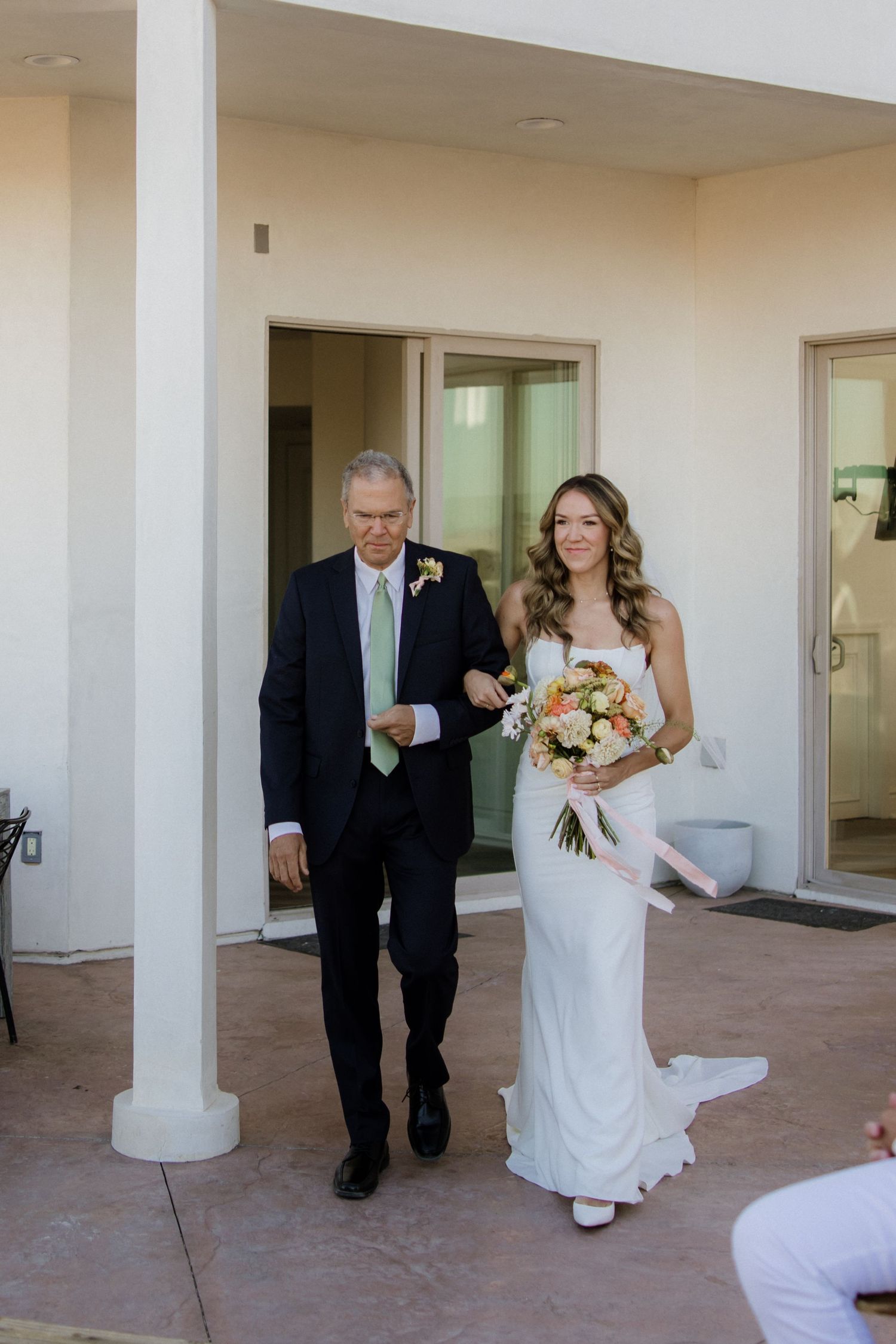 Wedding party participants wait behind pillars before ceremony in cream-colored venue hallway.