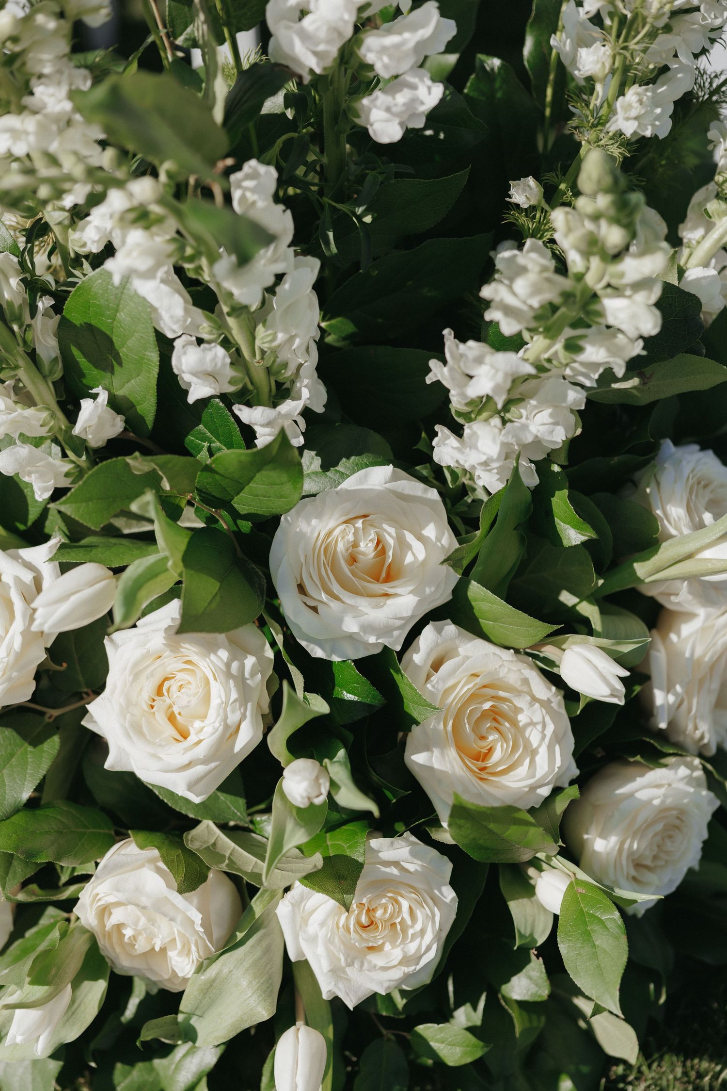 Close-up of lush white wedding floral arrangement featuring roses and snapdragons with green foliage.