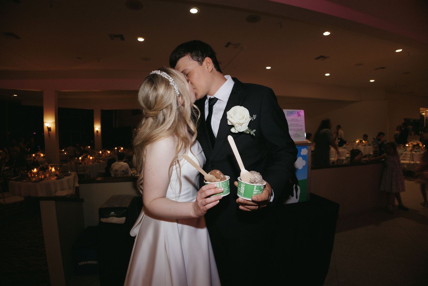 Bride and groom share a kiss while holding colorful dessert cups at wedding reception.