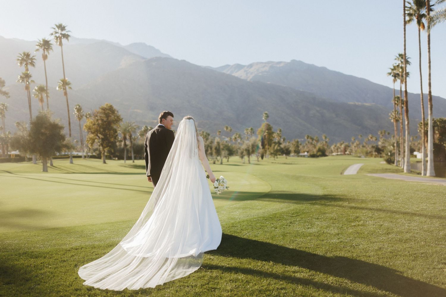 Bride and groom pose on golf course with stunning mountain backdrop in Palm Springs.