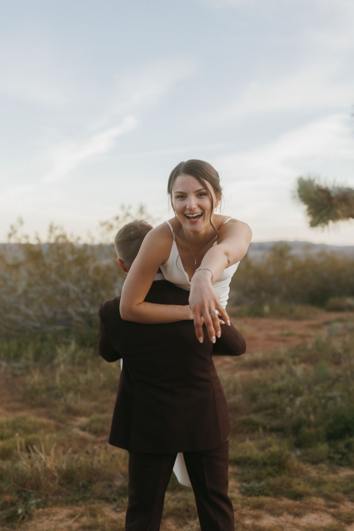 Joyful bride laughs as groom lifts her during playful outdoor desert wedding portrait session.