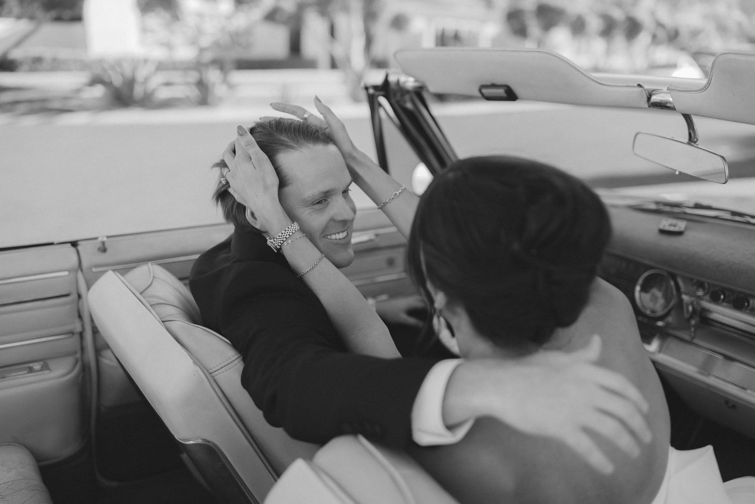 Black and white photo of a couple sharing a romantic moment in a vintage convertible car.