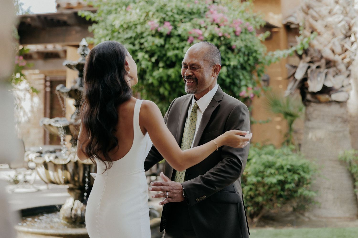 A joyful couple shares an intimate dance moment outdoors surrounded by lush greenery and stone architecture.