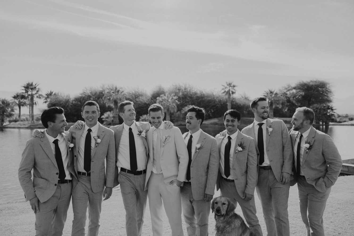 A group of groomsmen wearing light gray suits and ties pose together outdoors in a vintage black and white photograph.