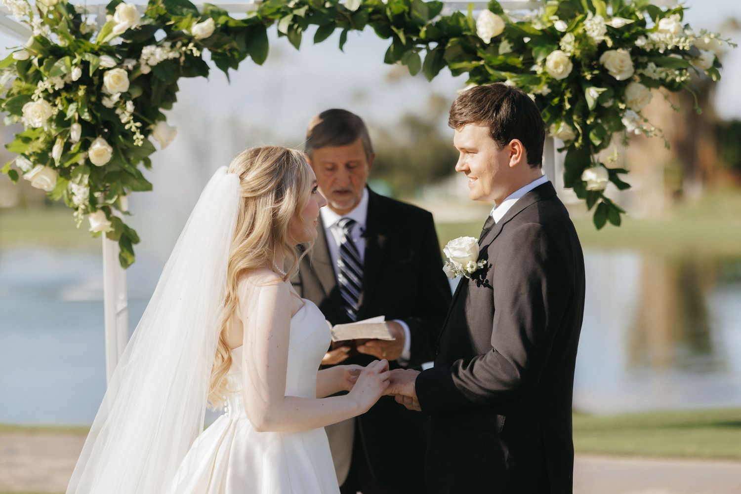 Bride and groom exchanging vows under floral arch at outdoor wedding ceremony.