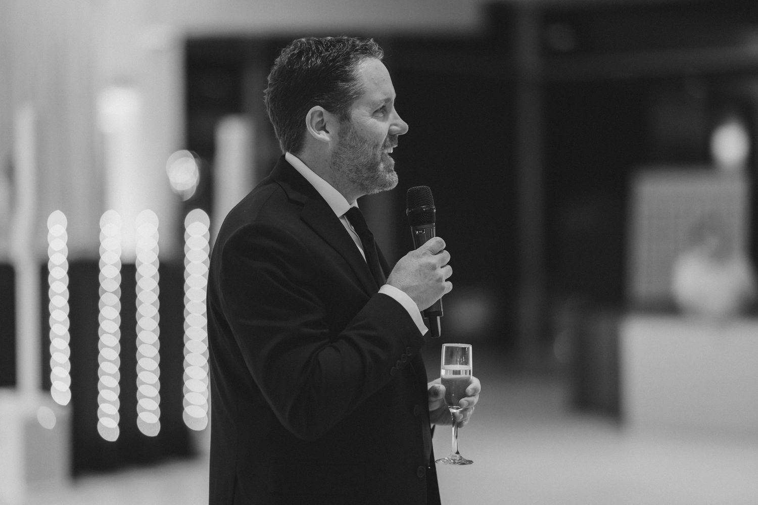 Black and white photo of a man in a suit giving a wedding toast while holding a champagne glass.