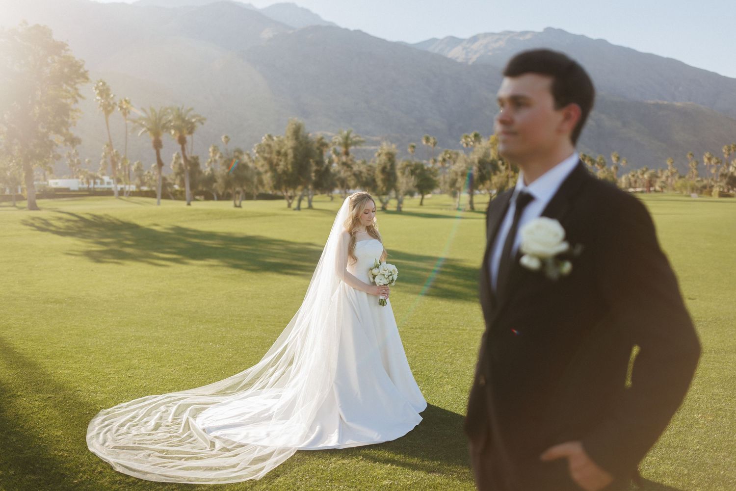 Bride in white gown with long veil poses on golf course with mountains in Palm Springs.