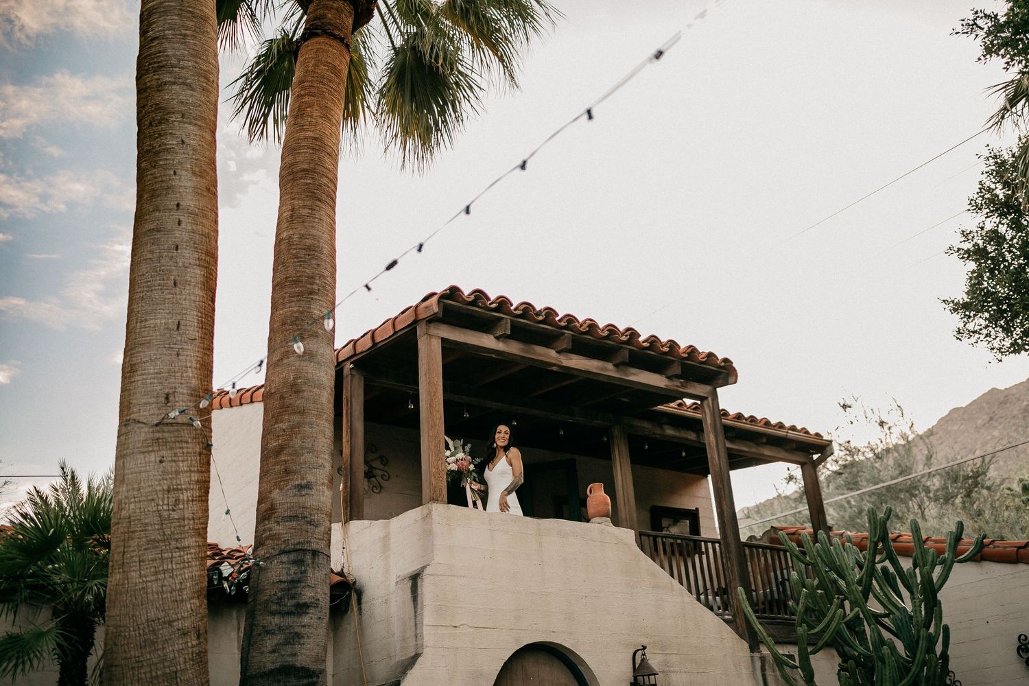 Spanish-style wedding venue with palm trees and string lights during golden hour.