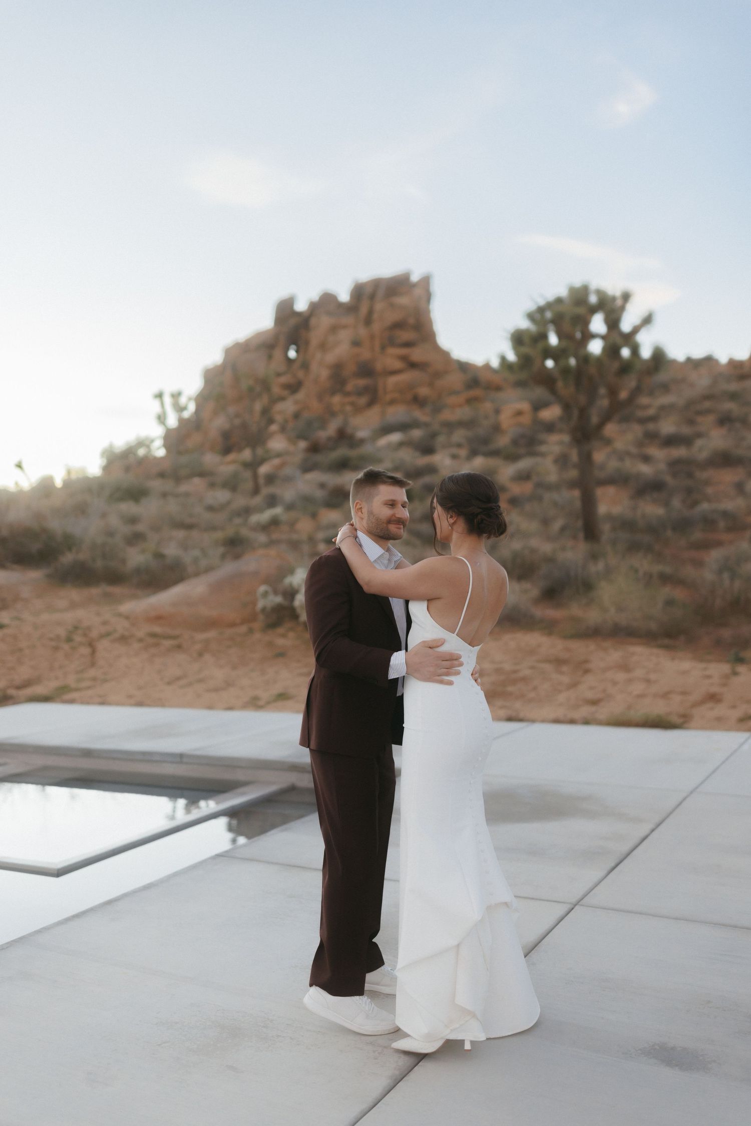 Bride and groom share their first dance on a modern patio with Joshua Tree rock formations at dusk.