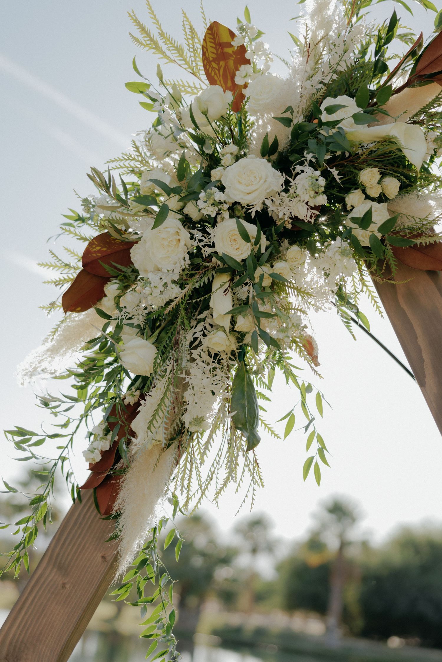 Elegant white roses and greenery floral arrangement adorning a wooden wedding arch with brown accents.