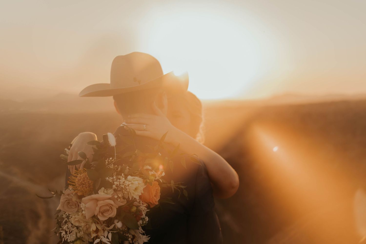 A glowing golden sunset casts warm light over a silhouetted figure walking through a rural field.
