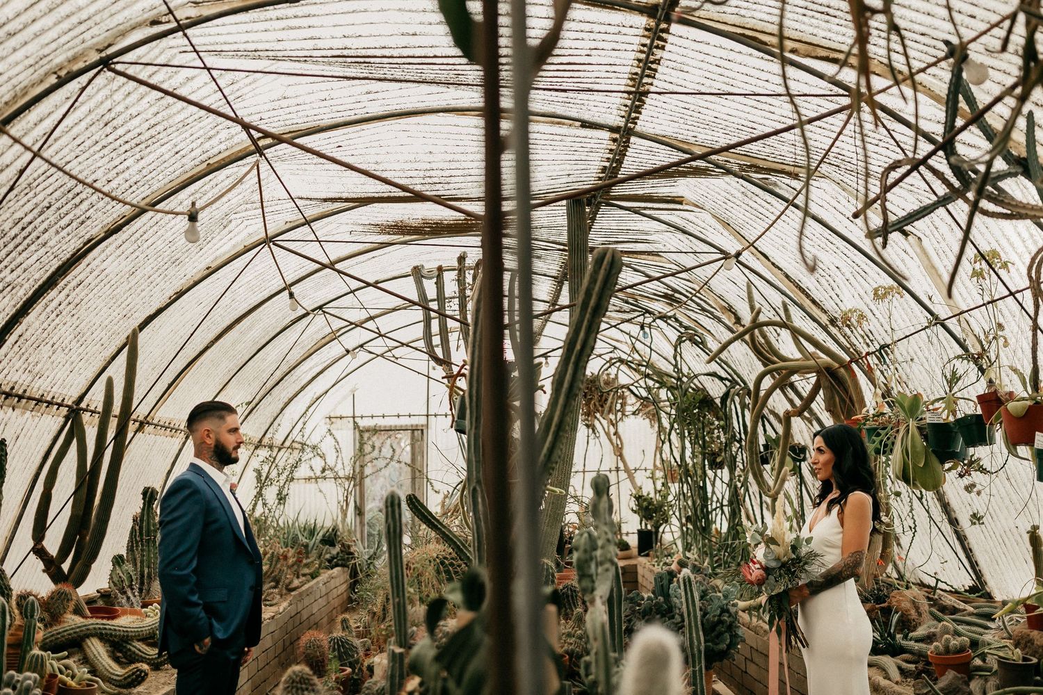 A greenhouse wedding ceremony setting with natural light streaming through transparent panels and lush greenery.