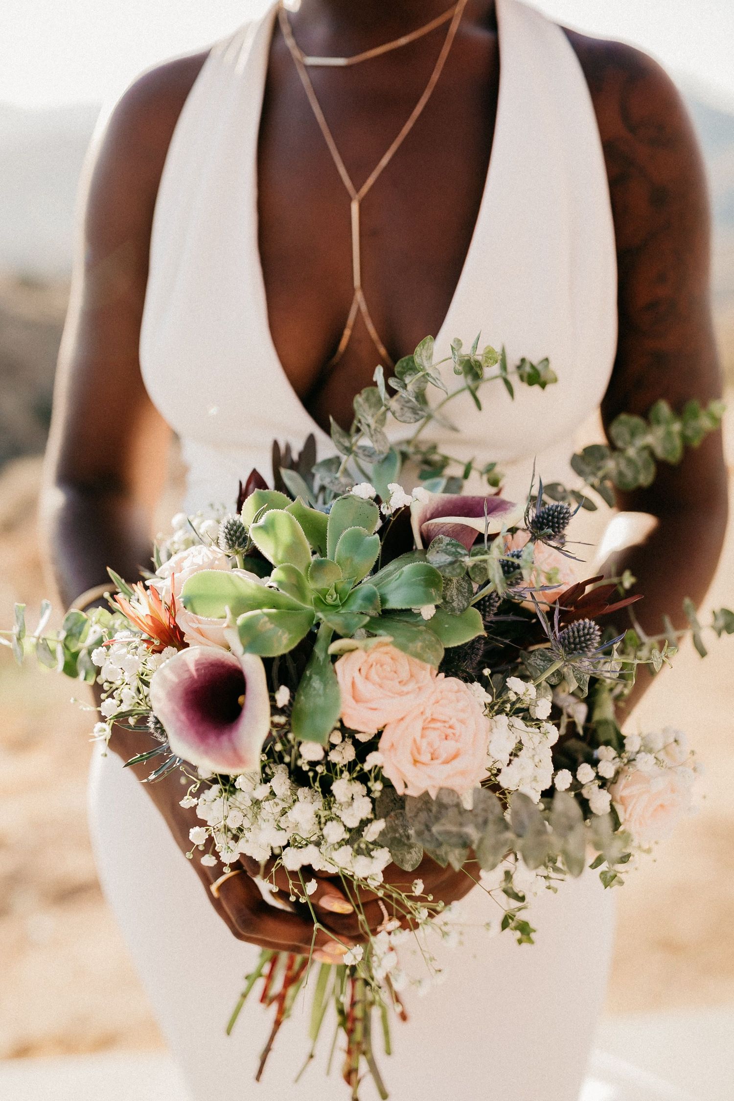 An elegant bridal bouquet with pink roses, calla lilies, and eucalyptus held against a white dress.