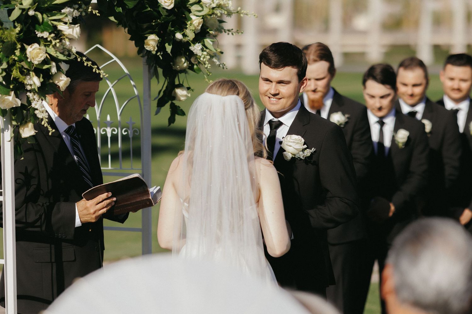 Bride and groom exchange vows at a floral arch during an elegant outdoor wedding ceremony.