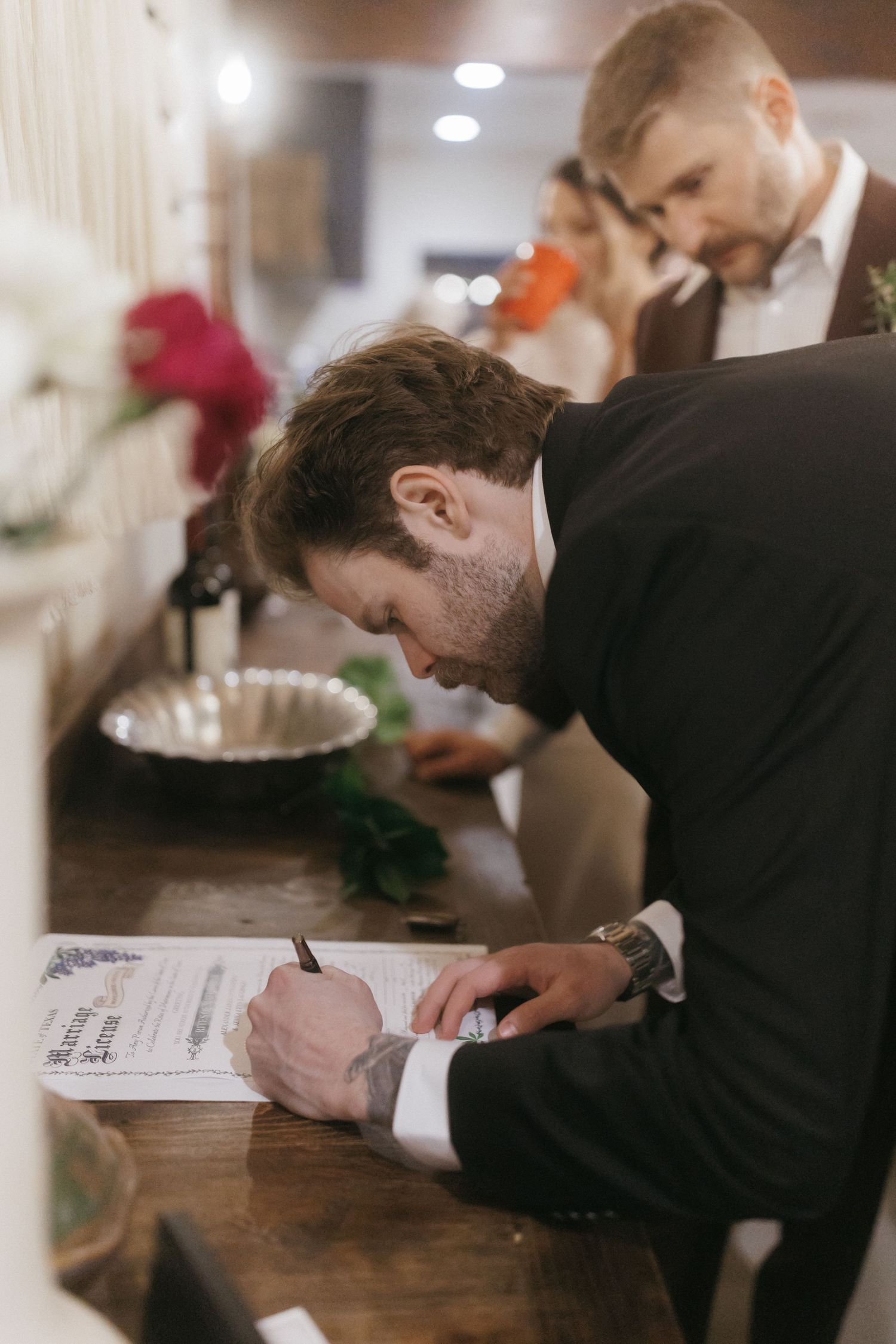 Guest signs wedding documents at a rustic indoor reception venue counter.