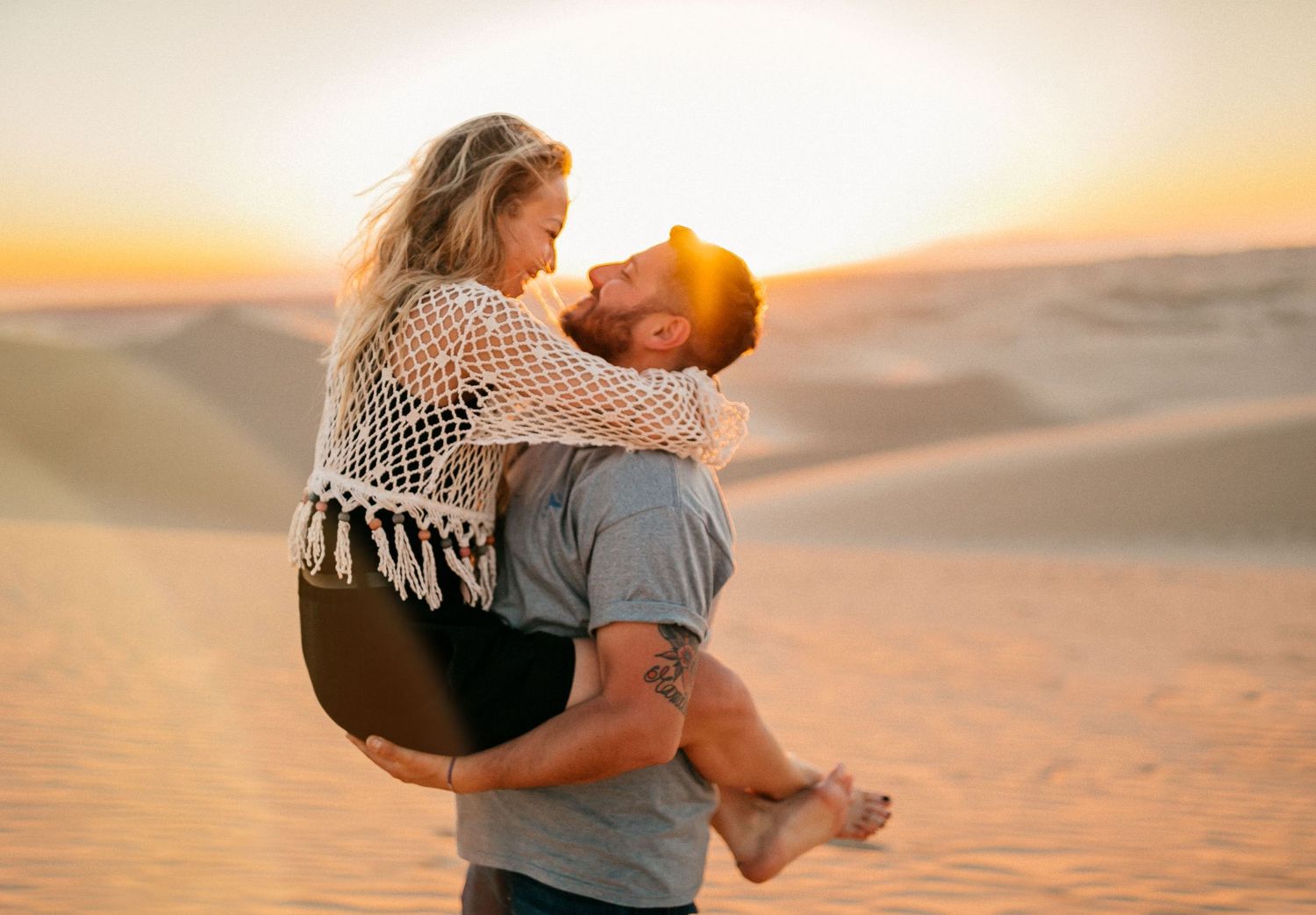 A couple sharing tender moments against a glowing desert sunset backdrop.