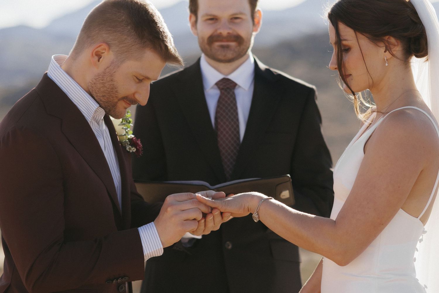 Groom placing wedding ring on bride's finger during outdoor desert ceremony.
