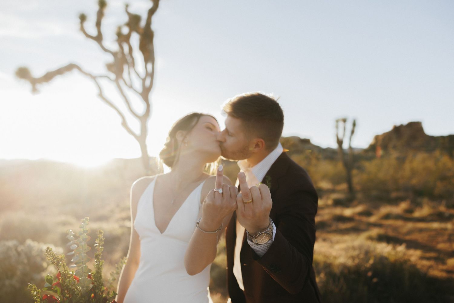 Bride and groom share a golden hour kiss among Joshua trees in desert setting.