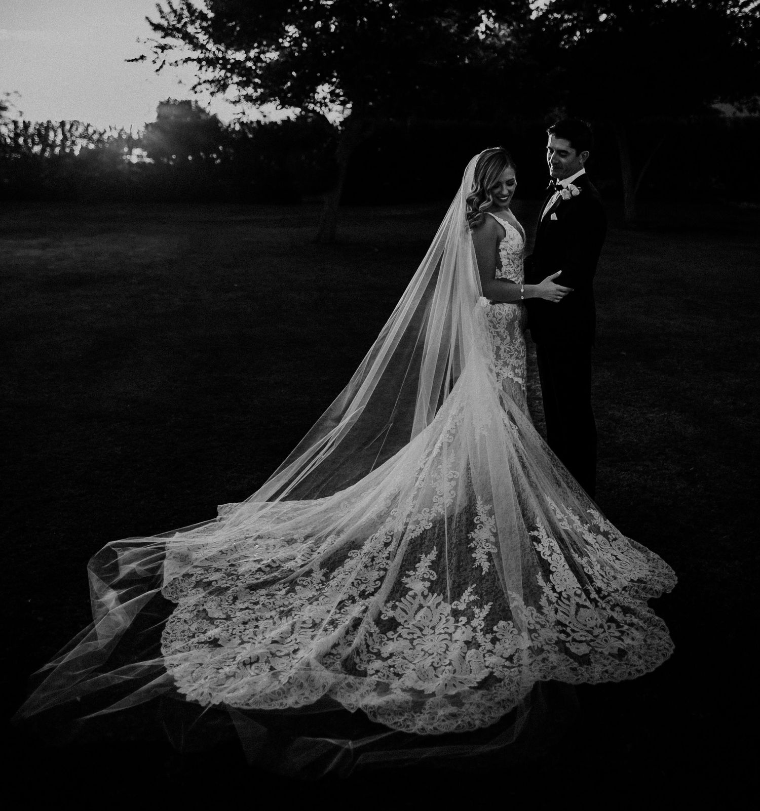 A wedding dress with a dramatic cathedral-length veil and intricate lace details shown in black and white.